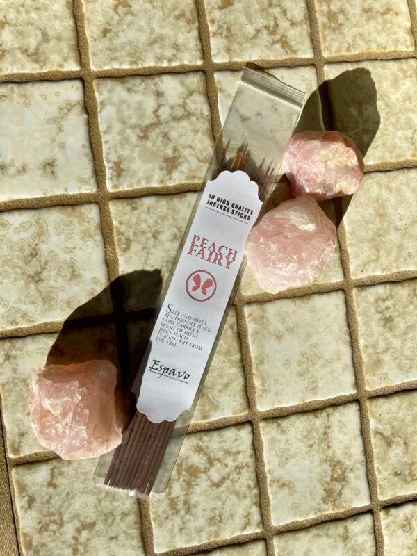 A pack of Peach Fairy Incense sticks on tan tiles surrounded by three chunks of rough rose quartz.